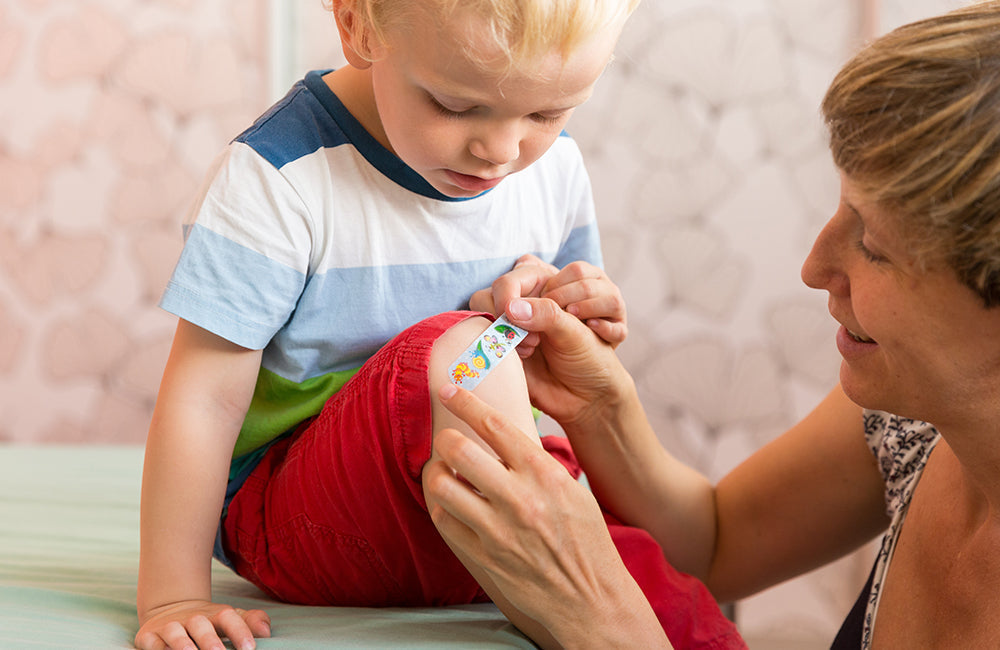 Eine Mutter klebt ein Kinderpflaster auf das Knie ihres Kindes.