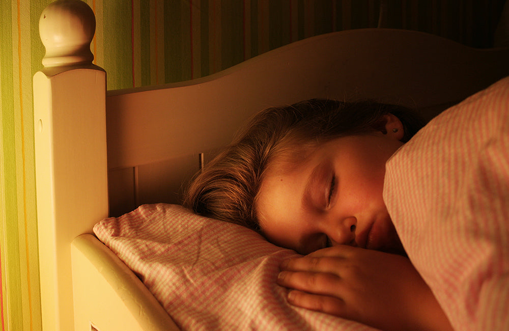 Ein Kind schläft in seinem Bett während ein Nachtlicht an ist.